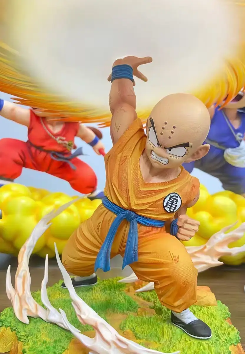 Collectible figure of a bald martial artist in orange, unleashing an energy blast with swirling effects, standing on a grassy base, with other characters in the background