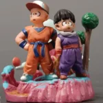 Alt text: Dragon Ball Krillin and Gohan detailed figurines in vibrant orange and purple battle suits, dynamic poses with colorful pink terrain and green trees background.